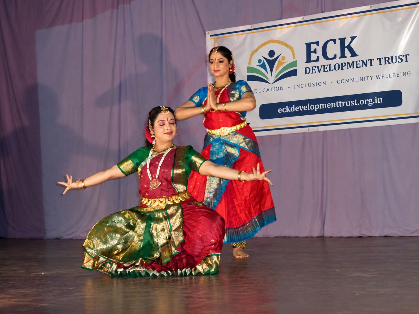 Two dancers performing on a stage beside an ECK Development Trust banner.