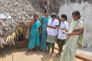 A small group talking together beside a thatched building.