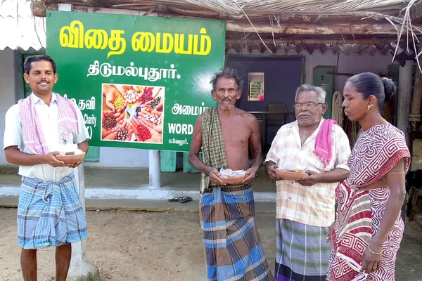 Two men holding a small packet beside seed-storage displays.