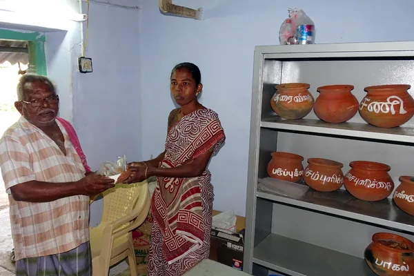 Two adults exchanging a seed packet beside a display of storage pots.
